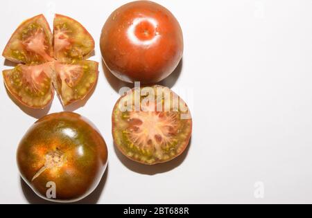 Set fresco di tre pomodori Kumato uno di loro aperto a metà e tritato su sfondo bianco Foto Stock