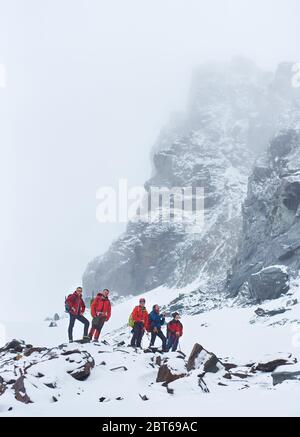 Turisti maschi con zaini e bastoni da trekking che si rompono durante l'escursione in montagna invernale. Gli alpinisti si schierano su rocce ricoperte di neve. Concetto di escursioni e turismo. Foto Stock