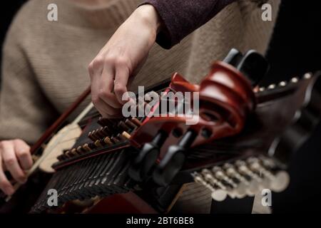 Donna musicista che aggiusta le tangenti della sua nyckelharpa in un primo piano sulle sue mani mentre si prepara per una performance dal vivo o prova Foto Stock