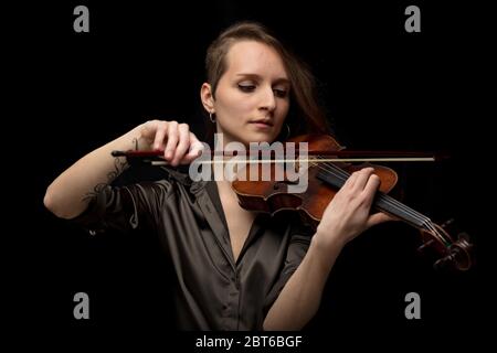 Violinista donna appassionata che suona musica classica su un violino barocco antico artigianale in un ritratto frontale su sfondo nero Foto Stock