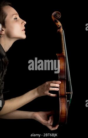 Donna musicista che tiene un violino barocco classico di profilo su uno sfondo scuro che mostra la struttura dello strumento Foto Stock