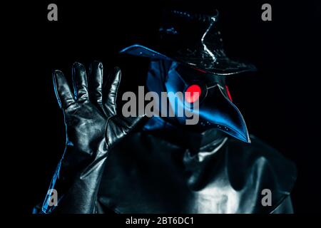 Uomo in costume medico peste con maschera corvo-come disapprovando senza gesto di segno di mano. Negando, rifiutando, non sono d'accordo isolato su sfondo nero Foto Stock