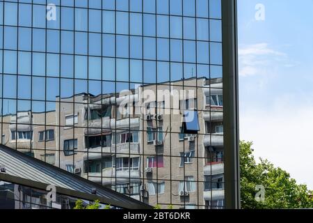 Vecchia casa residenziale a più piani si riflette in una parete a specchio di un edificio di uffici. Confronto tra la moderna facciata a specchio e l'obsoleto edificio in cemento Foto Stock