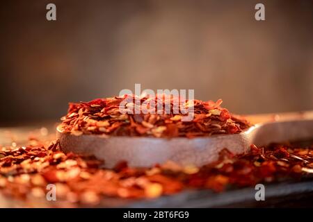 Fiocchi di peperoncino rosso caldo in cucchiaio di legno primo piano su un tavolo da cucina. Foto Stock