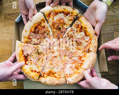 Mani di giovani che prendono fette di pizza dalla consegna scatola di cartone pranzo insieme, amici che condividono pasto a pranzo a casa, consegna del cibo concep Foto Stock