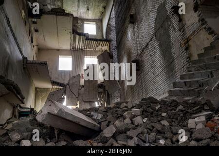 Edificio in cemento distrutto all'interno con un mucchio di detriti di costruzione in primo piano e grandi lastre di cemento appese sulla barra contro il muro posteriore Foto Stock