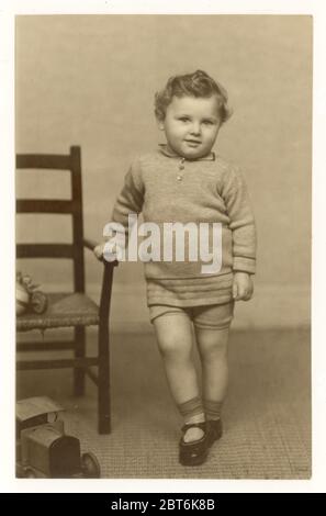Cartolina dei primi anni '900 di carino bambino giovane con capelli ricci, con un ponticello e shorts in maglia, circa primi anni '30, Regno Unito Foto Stock