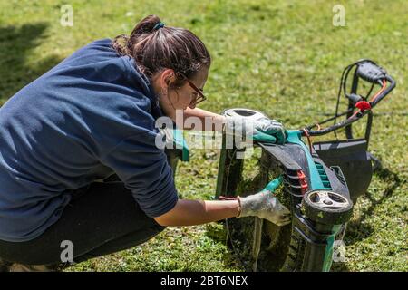 Giovane donna bianca che fissa il rasaerba in giardino Foto Stock