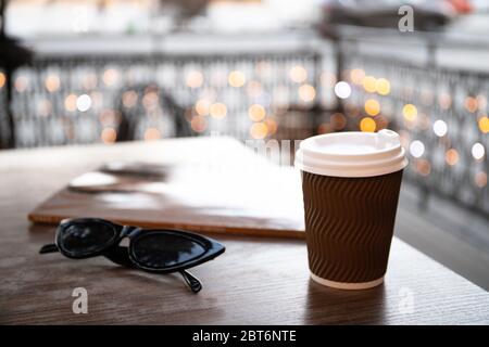 Tazza di carta con caffè e una rivista su un tavolo in un caffè Foto Stock