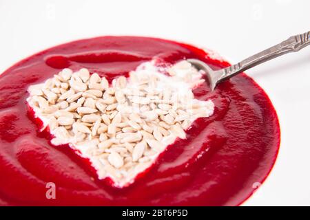 Zuppa di crema di barbabietole decorata con un cuore fatto di yogurt e semi di girasole mangiati con un cucchiaio d'annata Foto Stock