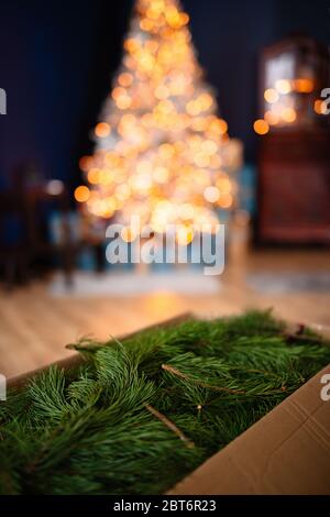 In Una Scatola Di Cartone Sono Rami Di Pino Verde La Scatola E Nella Stanza Sullo Sfondo C E Un Albero Di Natale Decorato Con Luci Foto Stock Alamy