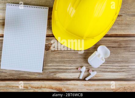 Costruzione di uffici di manutenzione, elmetto giallo con cuffie senza fili per notepad su tavola di legno vintage Foto Stock