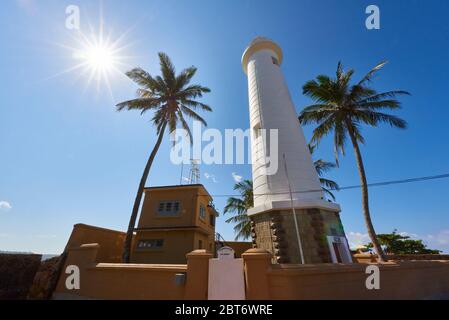 Foto diurna ad angolo basso del famoso Faro di Galle circondato da palme da cocco e il sole scoppiò, a Fort Galle, Sri Lanka. Foto Stock