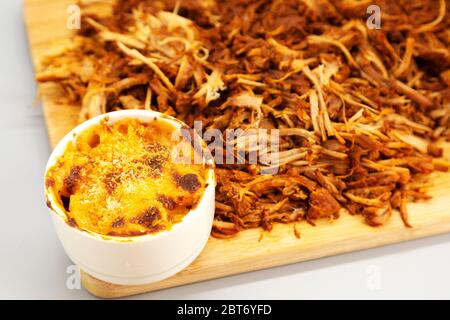 Maiale tirato homecoked servito sminuzzato su un asse di legno. Il piatto è servito con mac e formaggio. Foto Stock