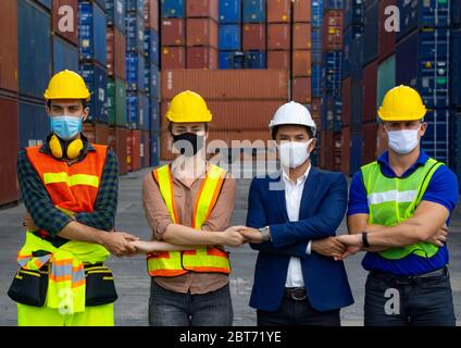 I lavoratori industriali o i tecnici che indossano le maschere di protezione Coronavirus o COVID-19 sono attraversati e si trovano di fronte al contenitore di spedizione. Foto Stock