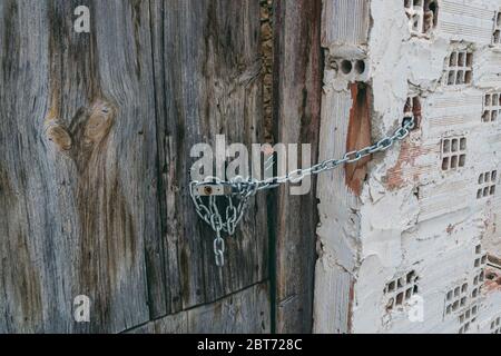 Cancello in legno arrugginito, catena e lucchetto appesi alla porta. Casa abbandonata. Vecchio cancello e lucchetto. Foto Stock