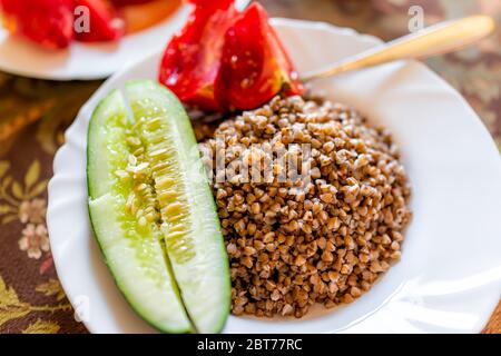 Macro closeup di marrone tradizionale arrosto grano saraceno grano saraceno grano prima colazione ucraino o russo cibo cotto pianura in piatto bianco su tavola con pomodori e. Foto Stock