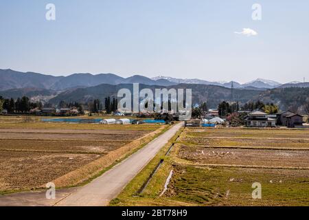 Toyama, Giappone strada campagna vicino Gifu prefettura con case tradizionali fattoria e campo marrone per raccolti e montagne in vista fotografato da tra Foto Stock