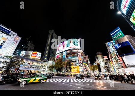 Shibuya, Giappone - 1 aprile 2019: Famoso attraversamento del crosswalk e traffico nel centro di Tokyo città con luci al neon cartelloni e pubblicità commerciale persone Foto Stock