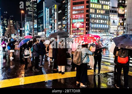 Shinjuku, Giappone - 1 aprile 2019: Persone con ombrelloni pioggia tempo in attesa di attraversare la passerella nel centro della città di notte durante la pioggia a Tokyo Foto Stock