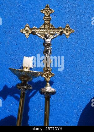Croce metallica per celebrazione cattolica con sfondo blu e un lampadario con candela bruciata a metà verticale Foto Stock