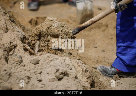 Dettagli con un operatore di costruzioni che utilizza una pala per caricare sabbia in una carriola. Foto Stock