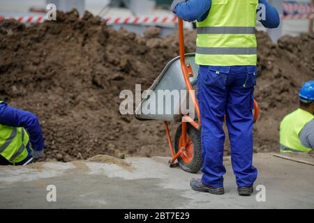 Dettagli con un operatore di costruzione che spinge una carriola su un cantiere. Foto Stock