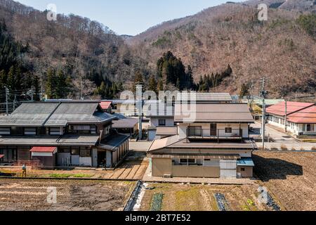 Hida, Giappone - 6 aprile 2019: Campagna con vista su terreni coltivati a riso nella zona rurale nella prefettura di Gifu con campo marrone in montagne alpi e tradizione Foto Stock