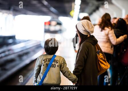 Utsunomiya, Giappone - 5 aprile 2019: Linea locale della piattaforma della stazione ferroviaria JR per Nikko con madre e bambino gente locale in attesa e in arrivo fari Foto Stock