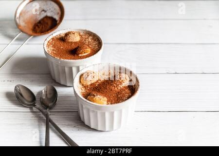 Delizioso dessert tiramisù con biscotti al cacao e savoyardi in vasi bianchi in ceramica su sfondo grigio Foto Stock