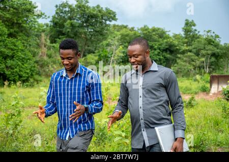 due giovani uomini d'affari africani, che discutono mentre camminano su un terreno Foto Stock