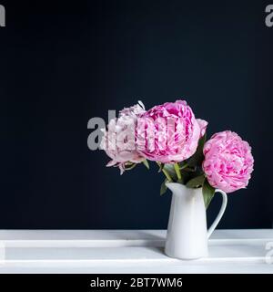 Tre peonie rosse in una caraffa bianca su sfondo nero. Spazio di copia. Spazio per il testo. Foto Stock