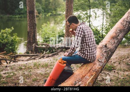 Ritratto giovane escursionista maschile mangiare mela. Turista alla foresta, sosta per riposare e mangiare mela. Uomo in forma mangiare una mela all'aperto nei boschi. Uomo caucasico Foto Stock