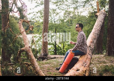 uomo che mangia una mela in escursione nella foresta. Escursionista che si prende pausa durante il trekking nella natura selvaggia. Viaggiatore maschile mangiare mela in seduta su albero caduto Foto Stock