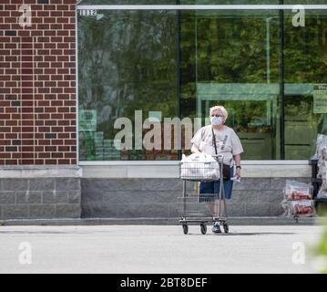 Berks County, Pennsylvania, USA- 19 maggio 2020: Lo shopper che indossa una maschera protictive spinge il carrello nel parcheggio del negozio di alimentari. Foto Stock