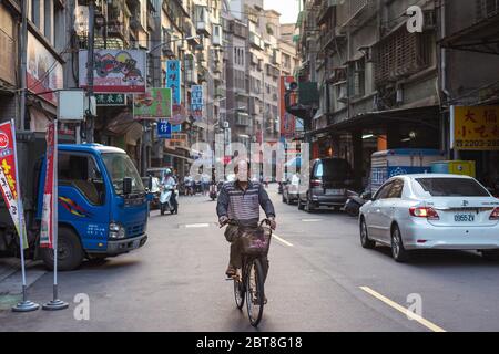 Taipei / Taiwan - 12 dicembre 2018: Uomo anziano in bicicletta lungo la strada panoramica con una moltitudine di edifici Foto Stock