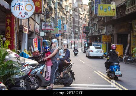 Taipei / Taiwan - 12 dicembre 2018: Giovane famiglia taiwanese con due bambini che cavalcano una moto in una bella strada Foto Stock