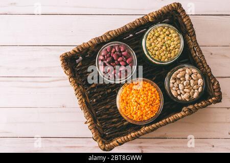 Lenticchie rosse, lenticchie verdi, fagioli rossi piccoli e fagioli di pinto in ciotole da vicino nel cesto di vimini, vista dall'alto con spazio di copia, look vintage. Foto Stock