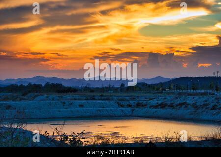 Questa foto unica mostra un cielo rosso acceso al tramonto riflesso in un lago. Sullo sfondo si possono ancora vedere le montagne di Hua Hin in Thailandia molto bene Foto Stock