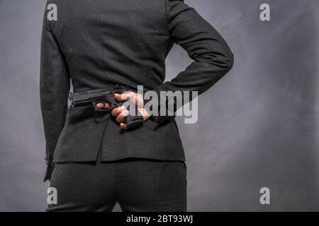 pistola in mano dietro la schiena di una donna in un vestito Foto Stock