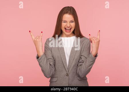 Ritratto di donna felicissima e sopravorato in tuta da lavoro che mostra il segno e gridando della mano rock and roll, che si presenta pazzo aggressivo con il gesto del diavolo corno. Foto Stock