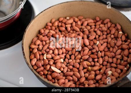 Le arachidi nella buccia vengono tostate in una padella. Le noci vengono fritte su un fornello in una vista dall'alto. Foto Stock