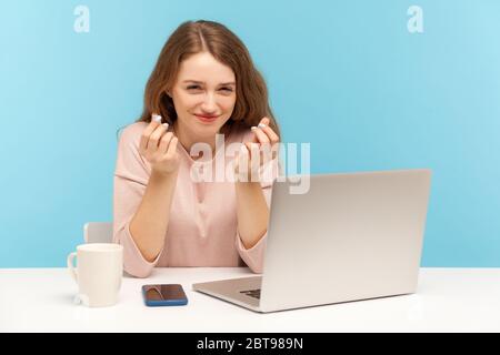 Ha bisogno di un salario più alto! Positiva giovane dipendente seduto sul posto di lavoro con il laptop e mostrando il gesto di denaro, chiedendo il pagamento, pianificare il reddito aziendale Foto Stock