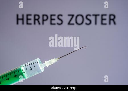 Questa illustrazione della foto mostra una siringa monouso con ago ipodermico, HERPES ZOSTER scritto su una tavola grigia dietro Foto Stock