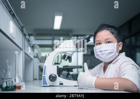 carino scienziato asiatico ragazzo indossare maschera e lavorare con il microscopio in laboratorio, scienza e concetto di educazione Foto Stock