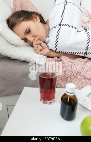 L'adolescente tosse. Gli intasa la bocca con la mano. Si trova sul letto. Frutta e medicina sul tavolo. Foto Stock