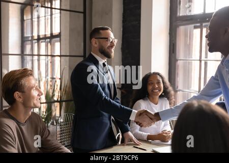 Uomo d'affari sorridente che indossa occhiali scuotendo le mani con partner d'affari diversi Foto Stock