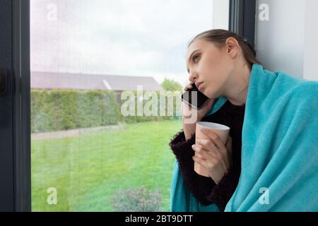 Guarda fuori la finestra. Prato verde. Nella mia mano tre tazza con tè alle erbe caldo. Parlare sul telefono cellulare. Foto Stock