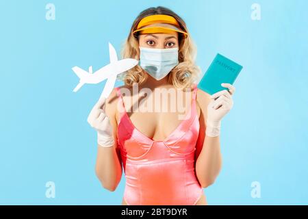 Gita estiva con covid-19. Donna in costume da bagno, con maschera igienica e guanti per prevenire il coronavirus contagioso, tenendo passaporto e volare aria Foto Stock