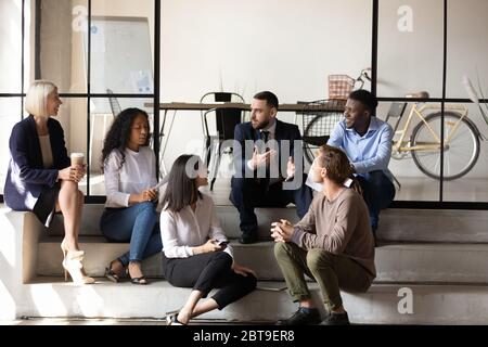 Diversi dipendenti chiacchierano, seduti sulle scale in un ufficio moderno Foto Stock